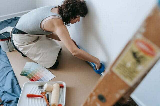 a woman applying painters tape around corners of the room with painter try and roller
