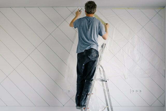 Man hanging up a plastic sheet to cut down on mess for article how to paint a popcorn ceiling