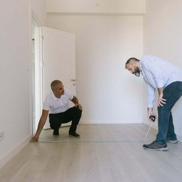 two people measuring a room for article how long does it take to paint a room?