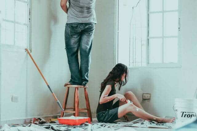 a man and woman painting the room. man is painting the wall and woman is painting baseboards