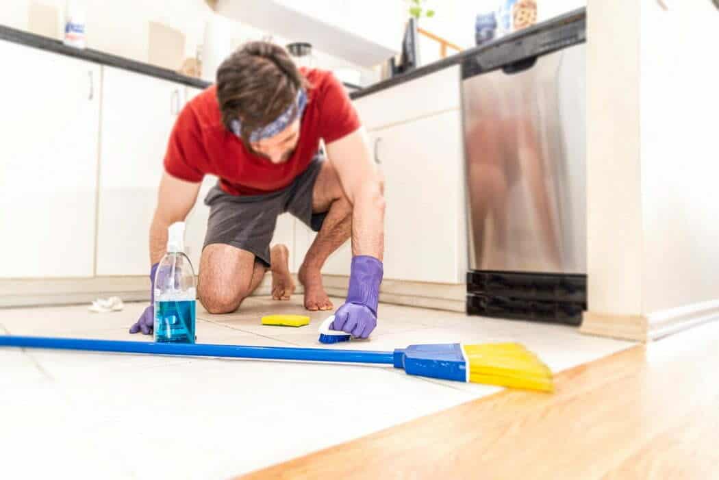 A man kneeling and cleaning his kitchen tiles