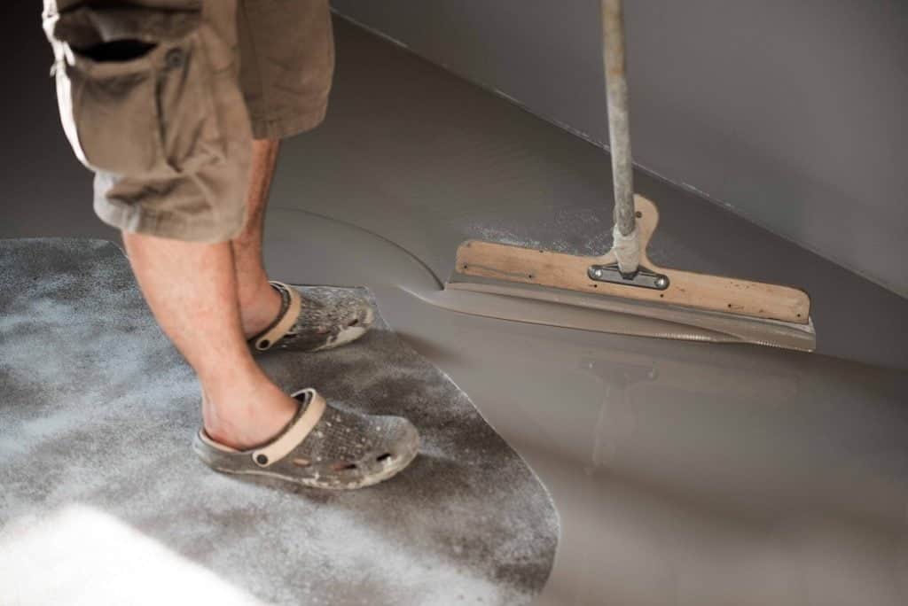 A man painting his indoor concrete floor with grey epoxy paint