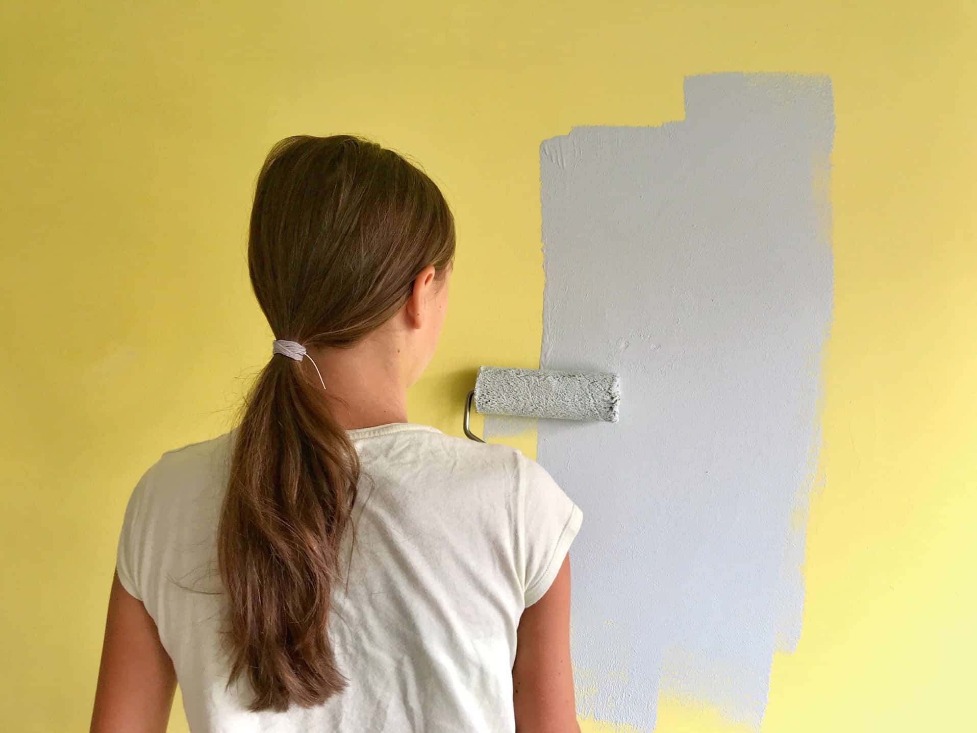 A woman painting her bedroom wall, for article how much does it cost to paint the interior of a house